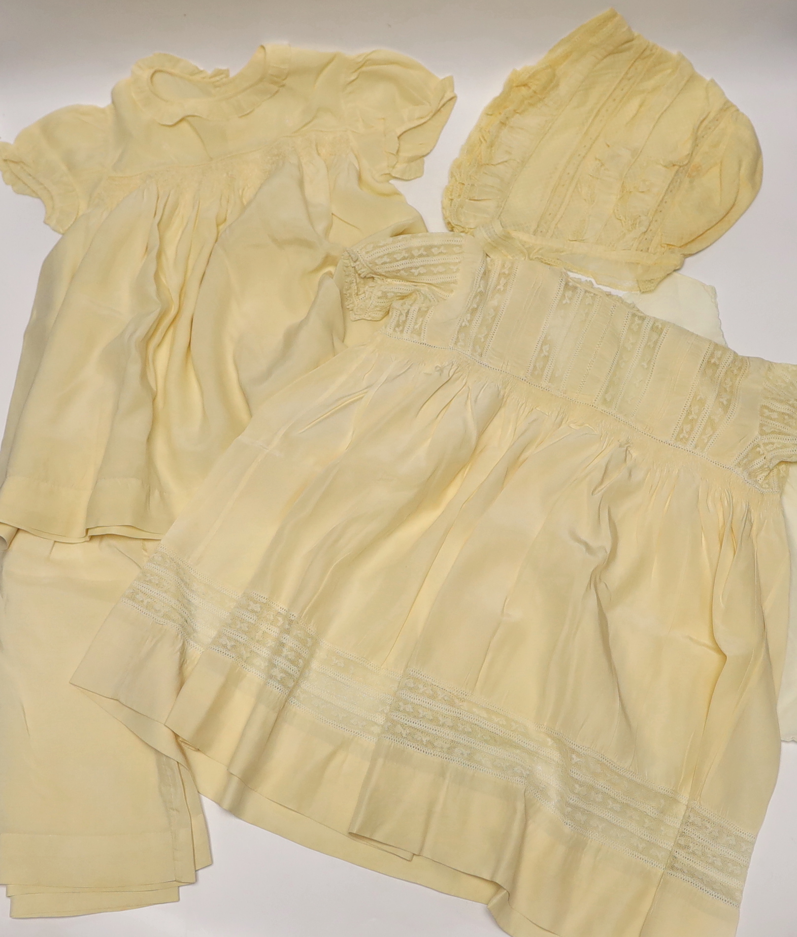 Two 19th century silk baby gowns, a ladies lace trimmed bonnet, a black satin and lace maids apron, various tatting tape lace and other table mats, etc.